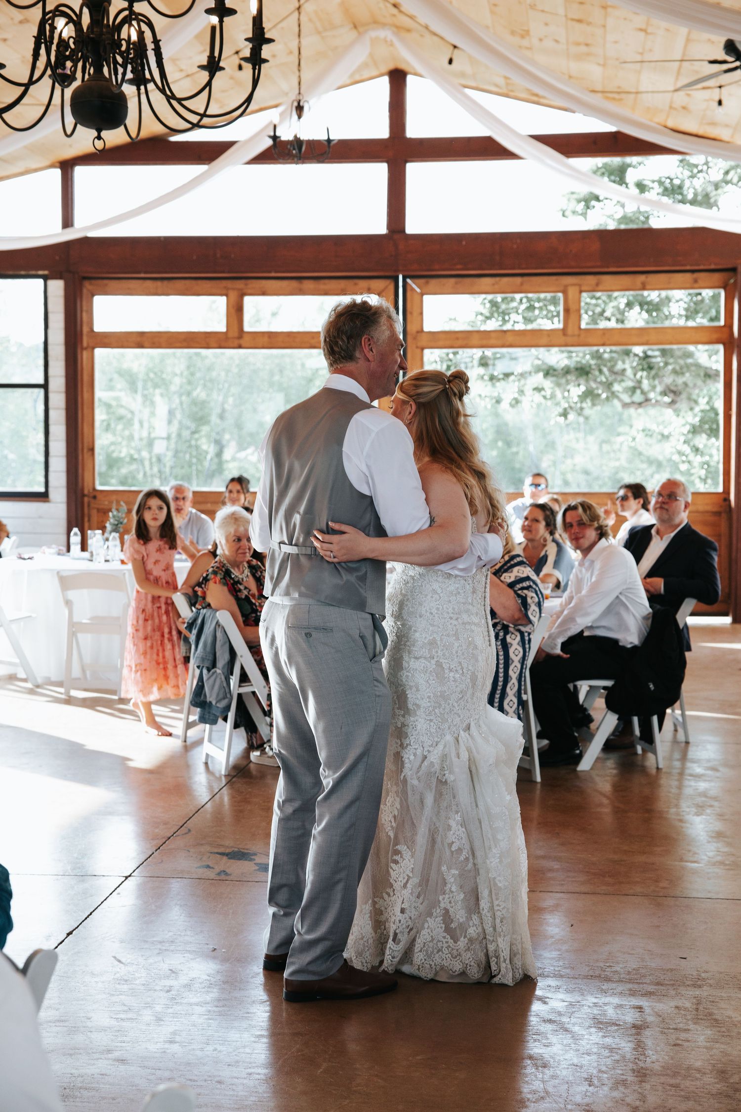 A couple shares their first dance at a rustic wedding reception with guests watching from decorated tables.