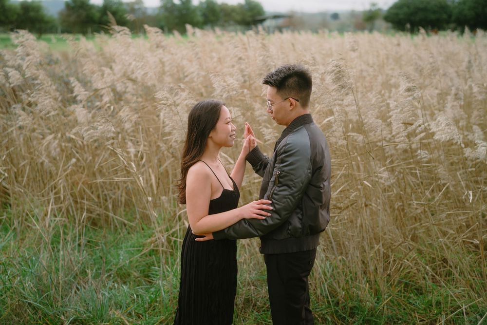 Romantic couple embraces in tall golden grass field during outdoor photo session at sunset.