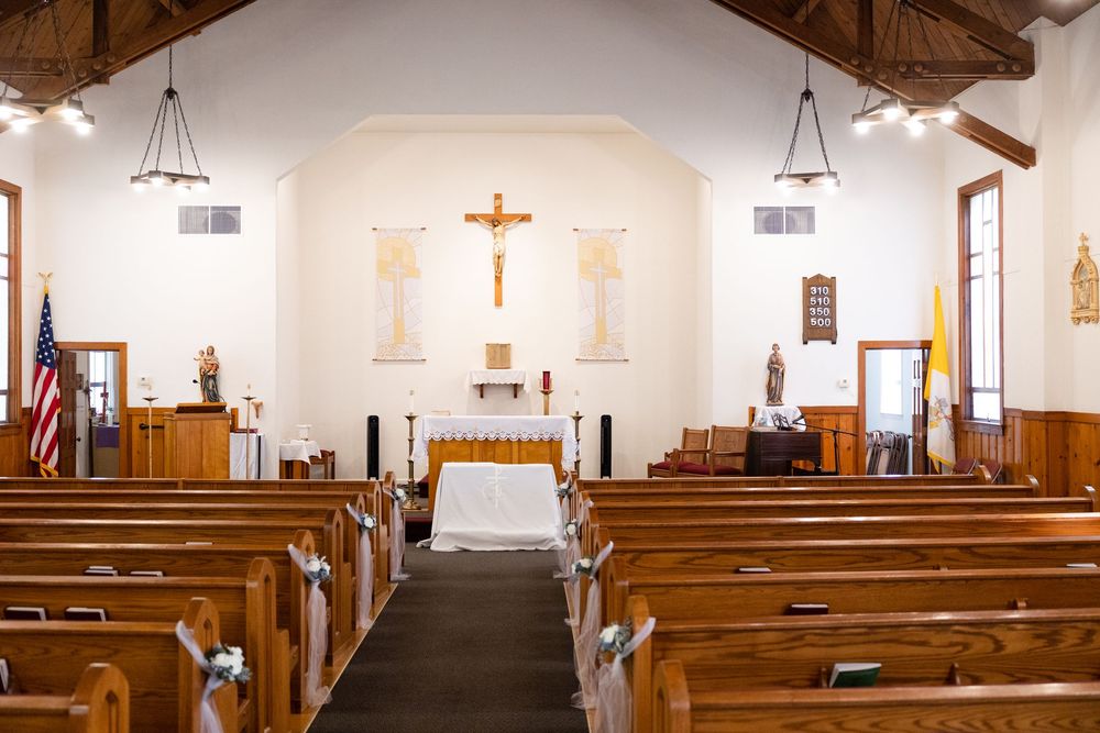 Interior of a Catholic church with wooden pews, altar, and crucifix under exposed wooden beam ceiling.
