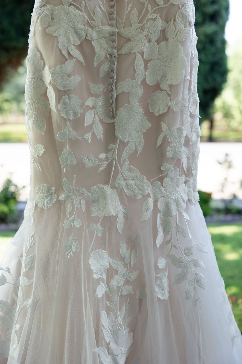 Close-up detail of delicate floral lace appliques on a light-colored wedding gown in natural outdoor lighting.
