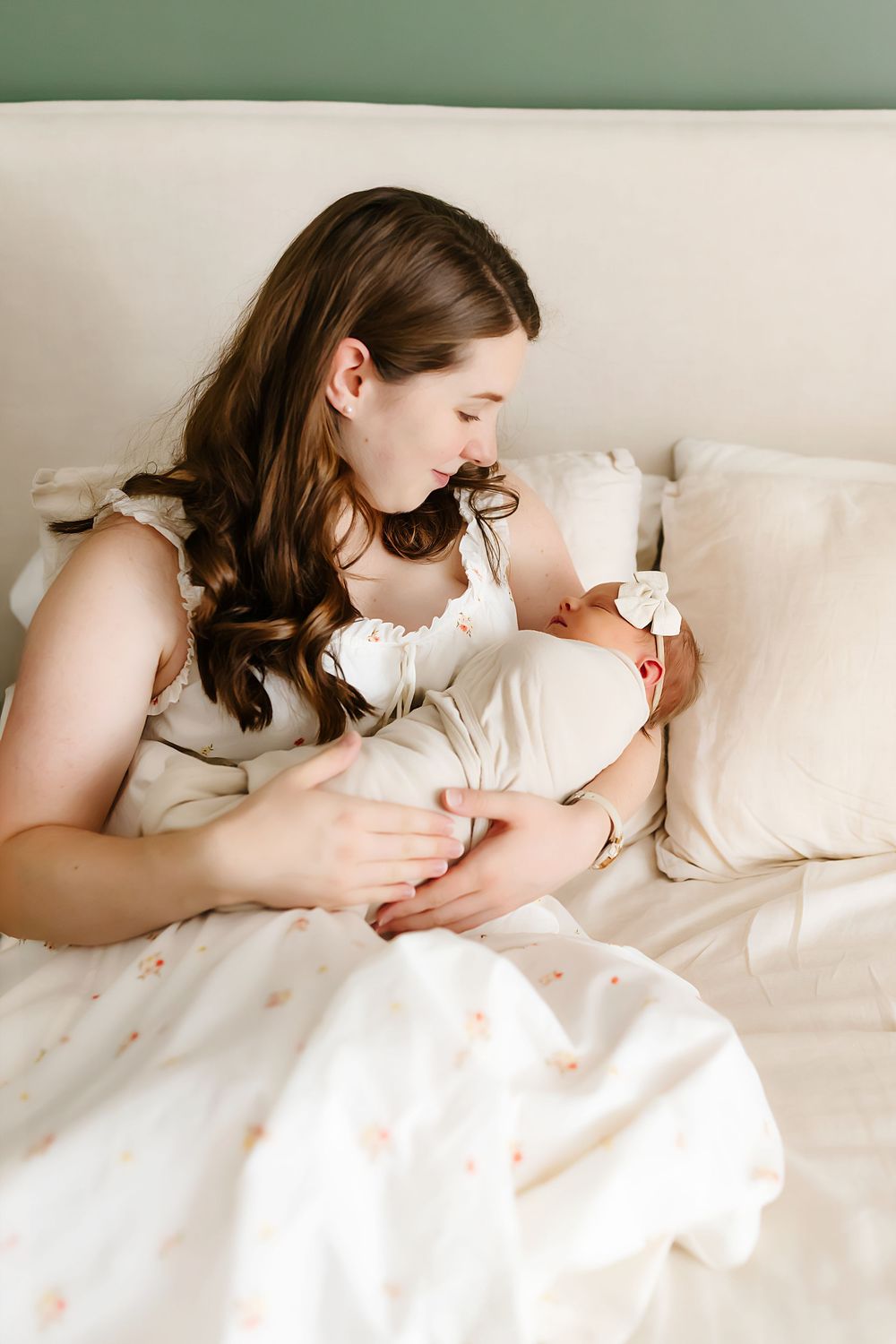 A gentle parenting moment on a white bed with soft pillows and linens in natural lighting.