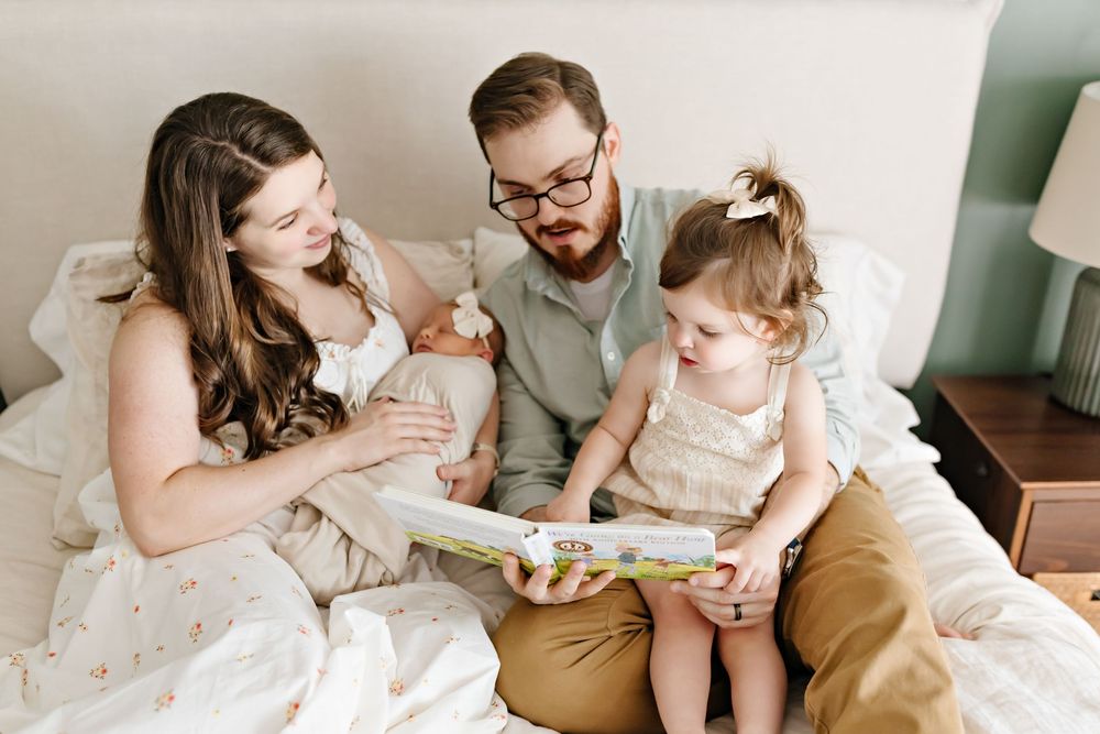 A family sits together on a bed reading a book and sharing a tender moment together.