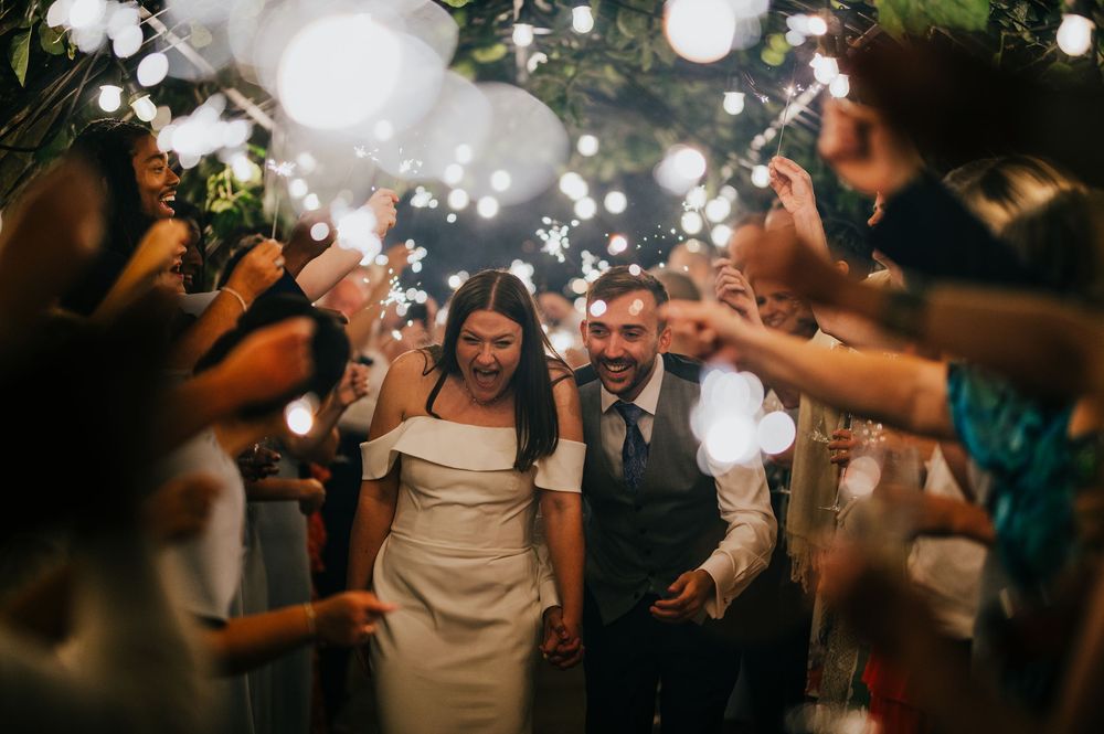 Wedding couple walking through bubbles at night during their reception celebration with guests on both sides.