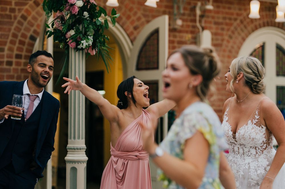 Guests share a joyful moment together during a wedding celebration at a brick venue with arched windows and floral decor.