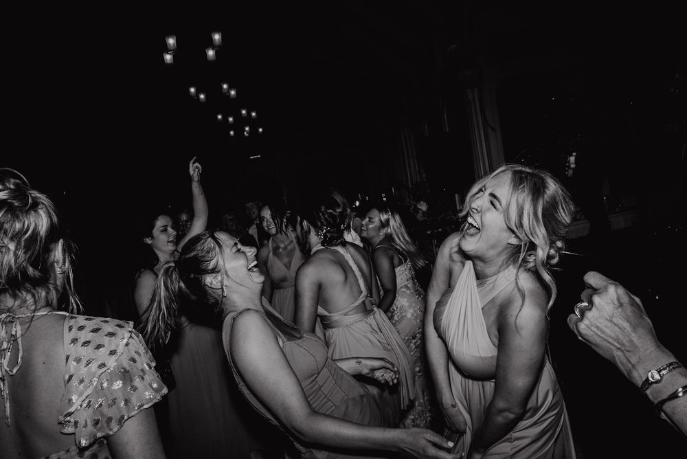 Black and white photo of people dancing and celebrating enthusiastically at a nighttime party with small lights visible above.