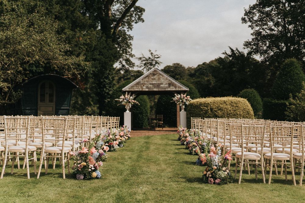 White wooden chairs arranged in rows on a grassy hill create an elegant outdoor wedding ceremony setting.