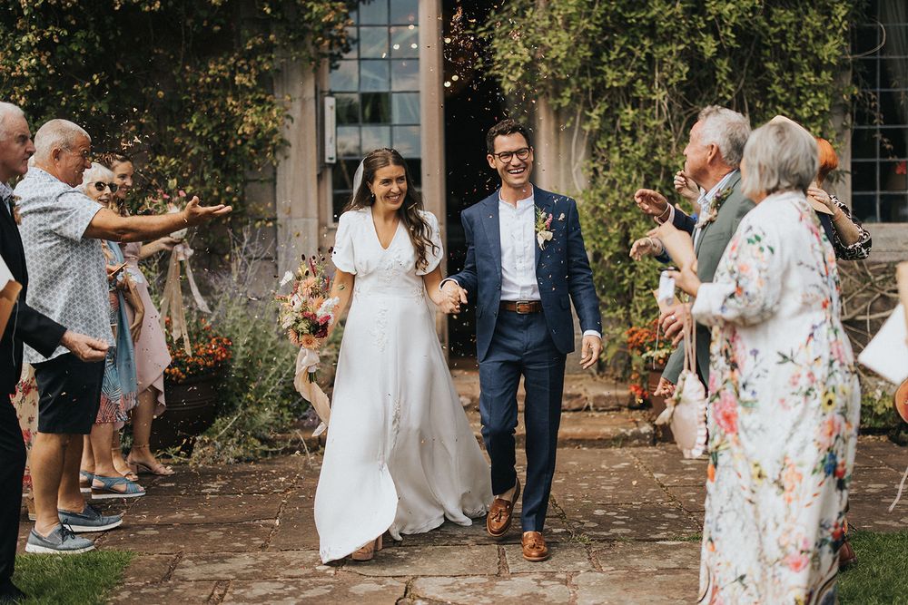 Bride in flowing white dress twirls and dances joyfully in an outdoor garden setting during a wedding celebration.