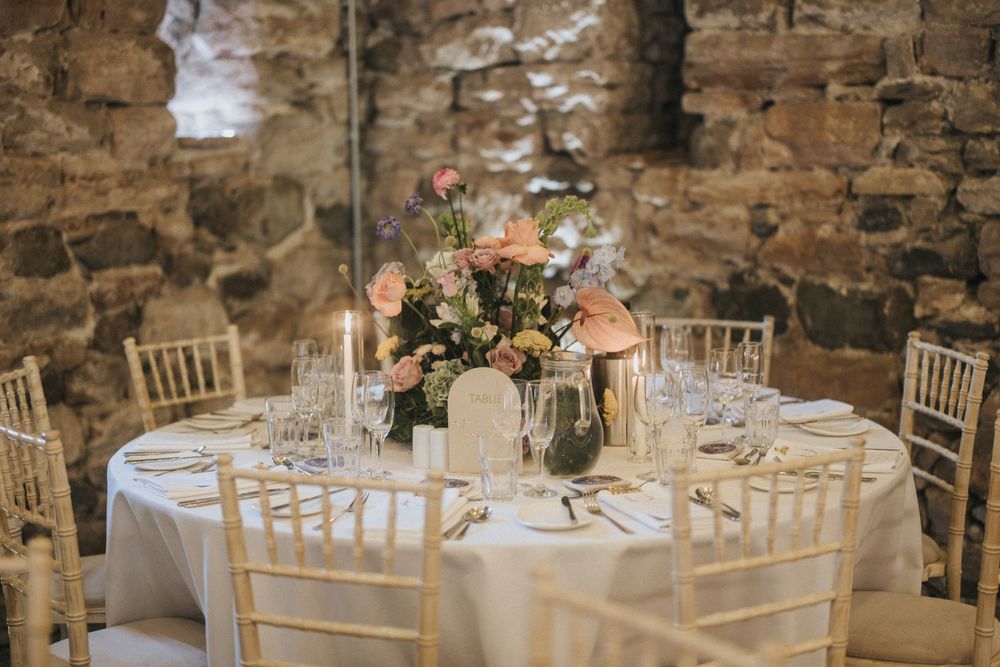 Elegant wedding reception table with pink floral centerpiece and chiavari chairs in rustic stone venue.