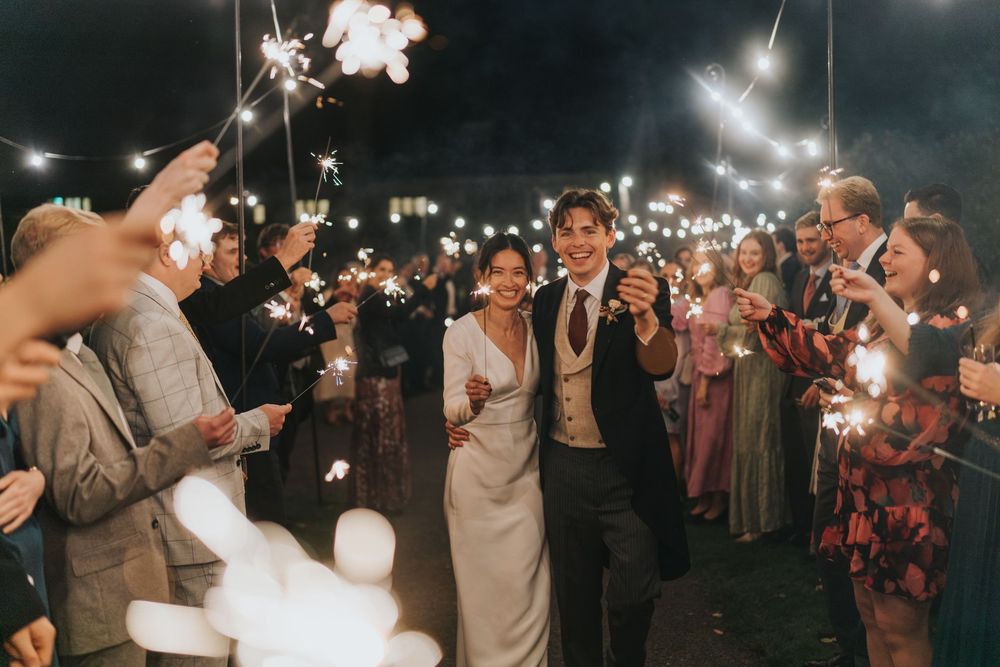 Wedding guests create a magical sparkler sendoff tunnel for the newlyweds at a romantic outdoor nighttime celebration.