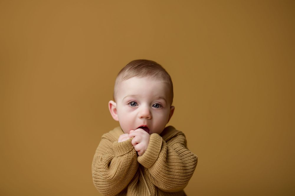 Baby wearing a tan knit sweater makes different adorable expressions in a series of connected photos.
