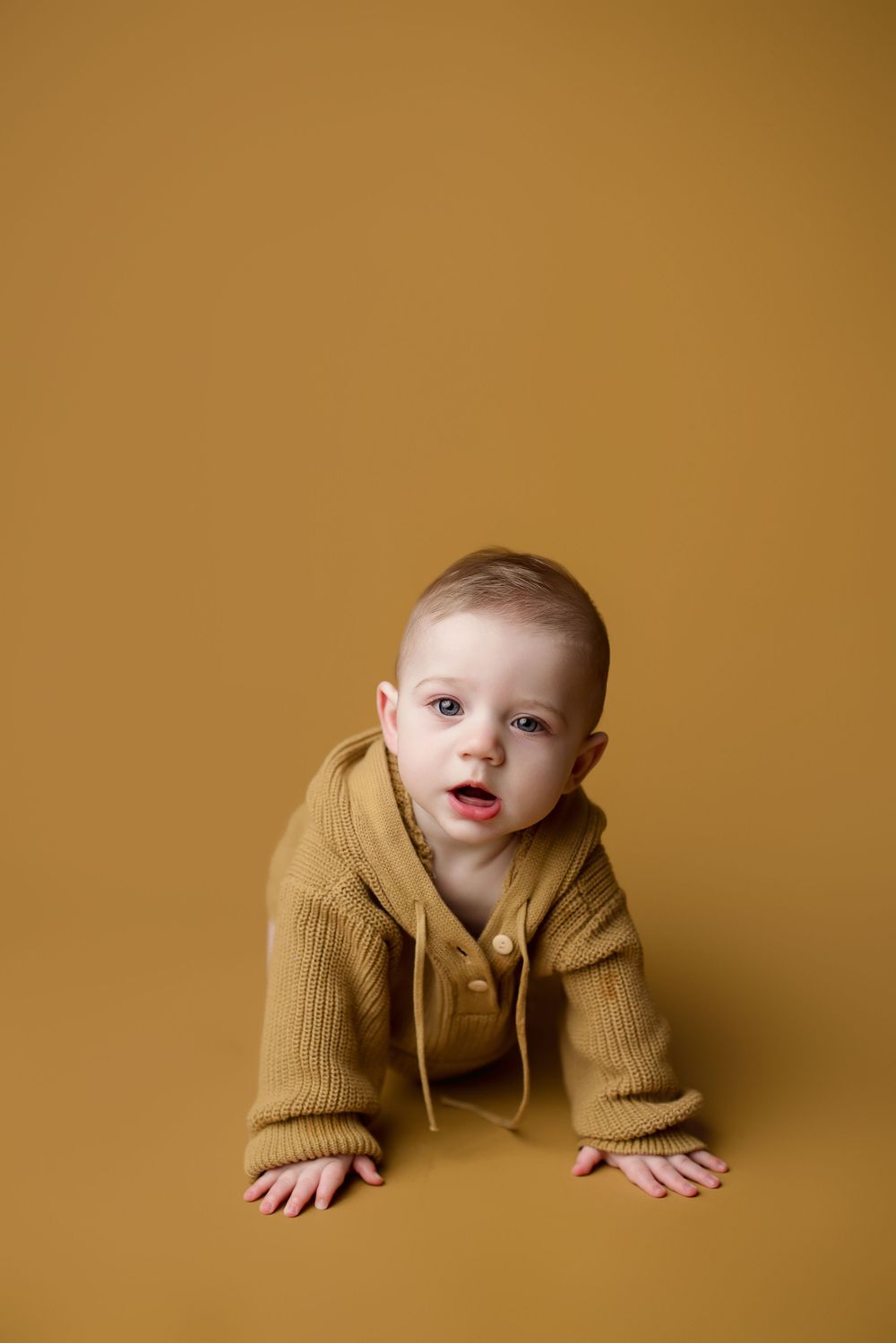 Baby wearing warm mustard-colored sweater poses against golden backdrop in creative studio photography sequence.