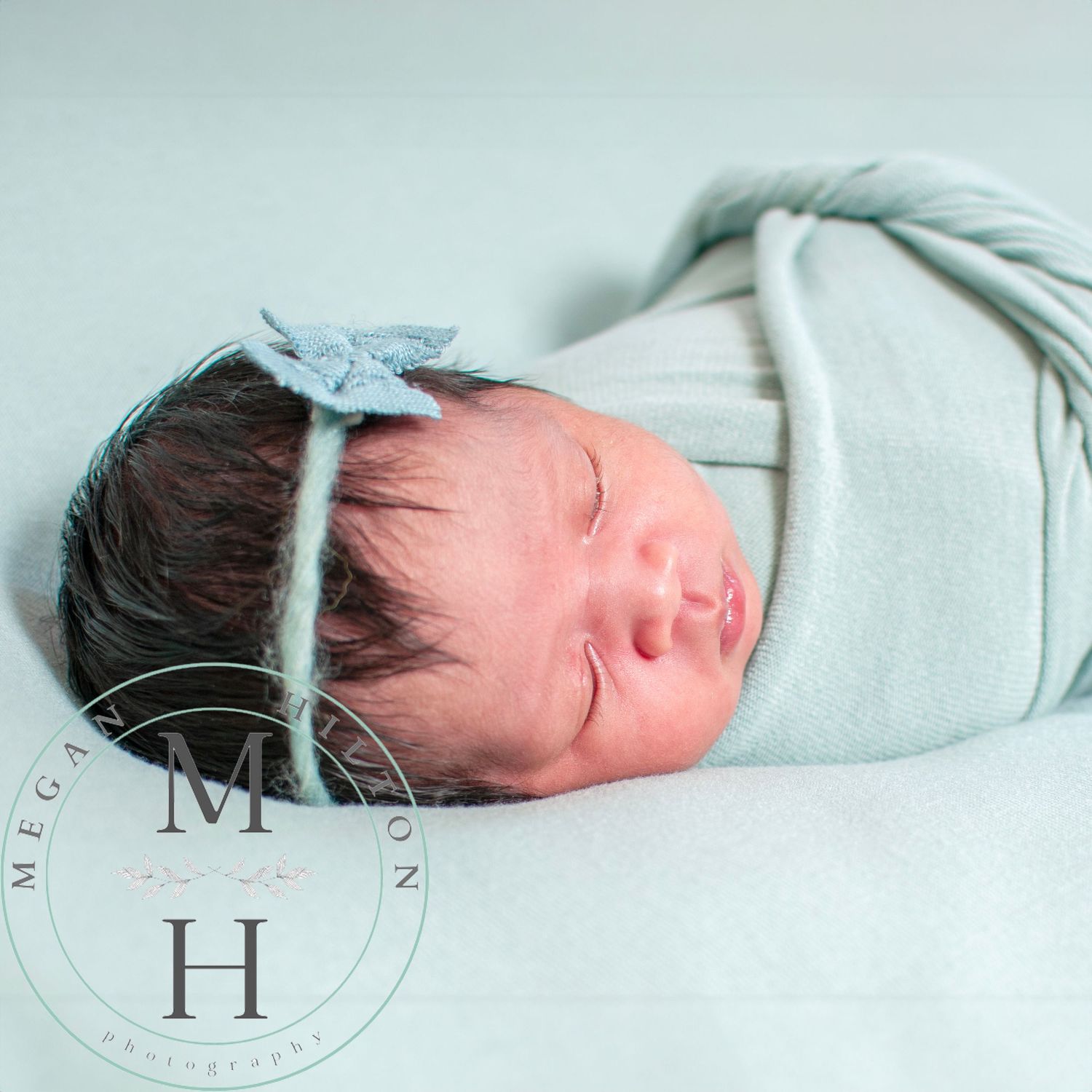 Sleeping newborn baby wrapped in soft mint green swaddle with matching headband, photographed from above.
