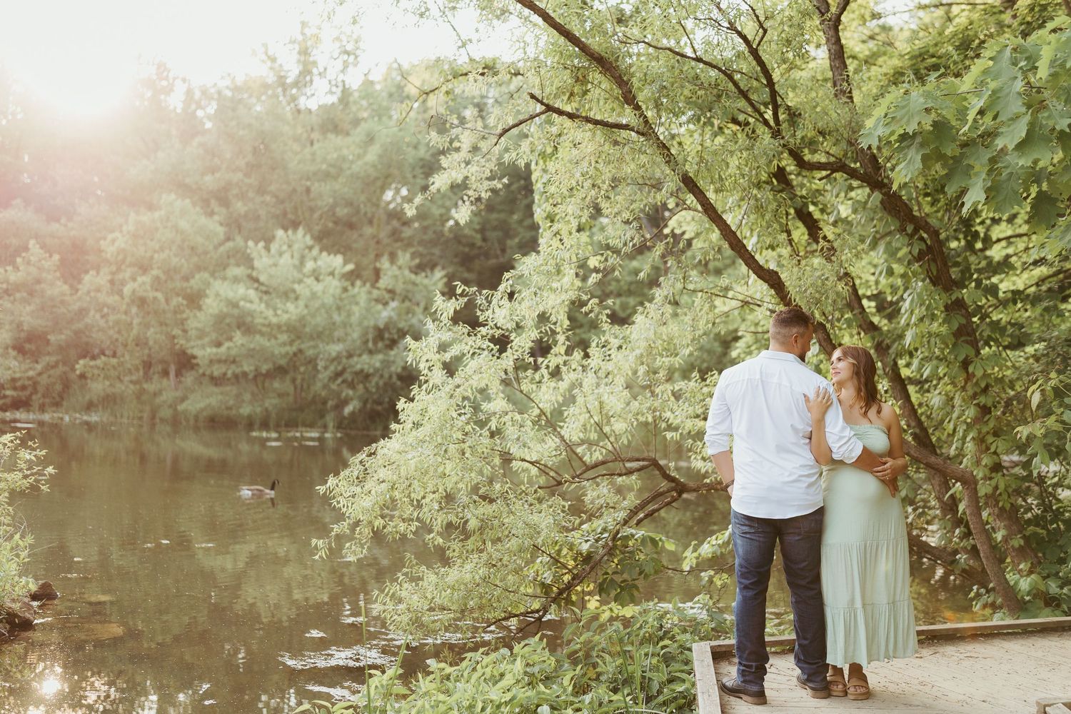 maternity photos in pittsburgh pennsylvania by ash coniglio photography, couple poses in front of greenery surrounded pond and gold sun haze