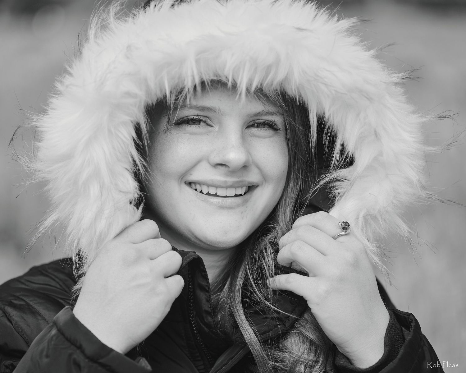 High School senior female wearing quilted winter coat holding fuzzy white fur hood over her head for closeup photo on hot day in May.