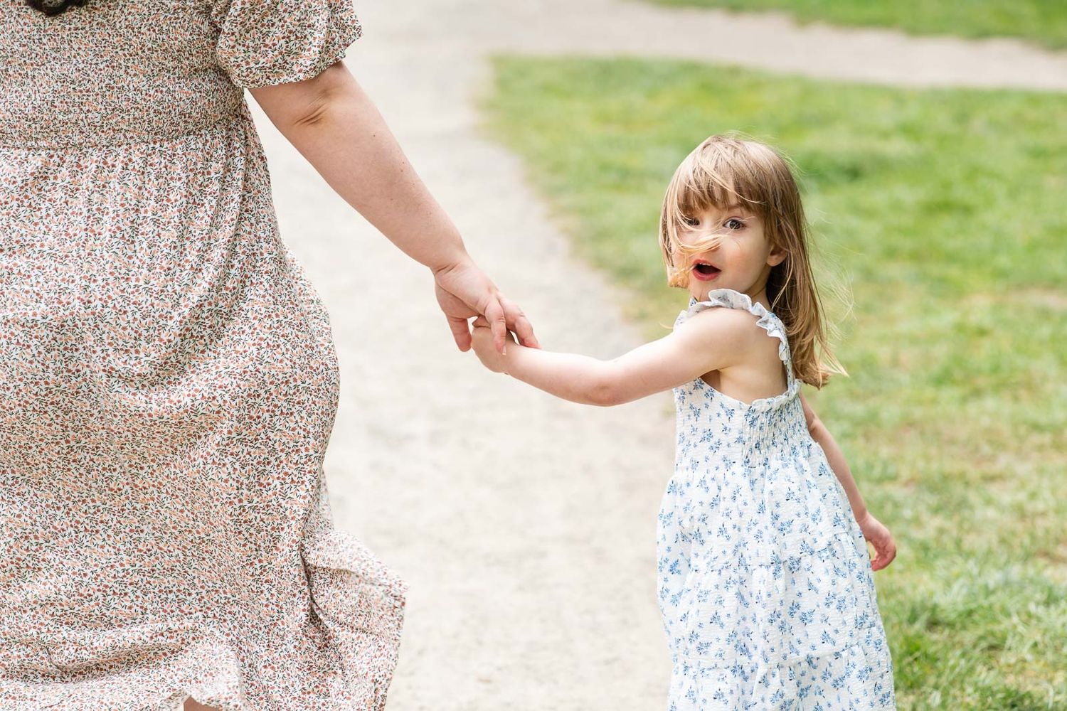 Daughter holding moms hands and looking back towards the camera.