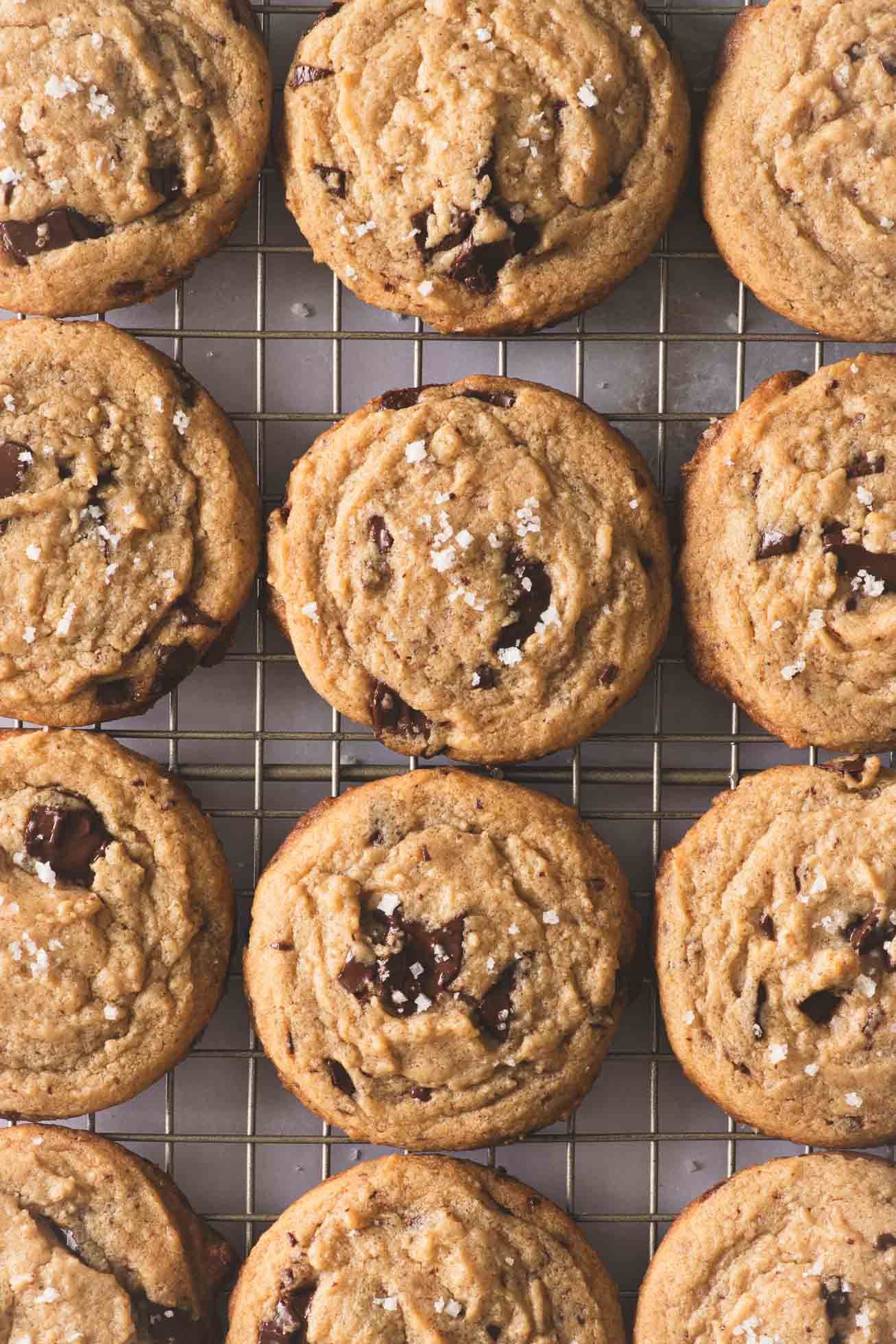 Homemade chocolate chip cookies with sea salt cooling on a wire rack with golden brown crispy edges.