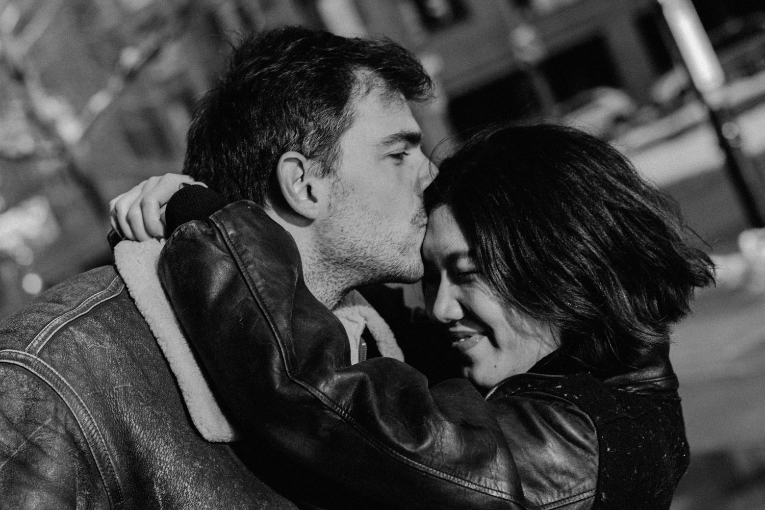 black and white photo with the boyfriend kissing her forehead and she is closing her eyes, both with a hard light in their faces