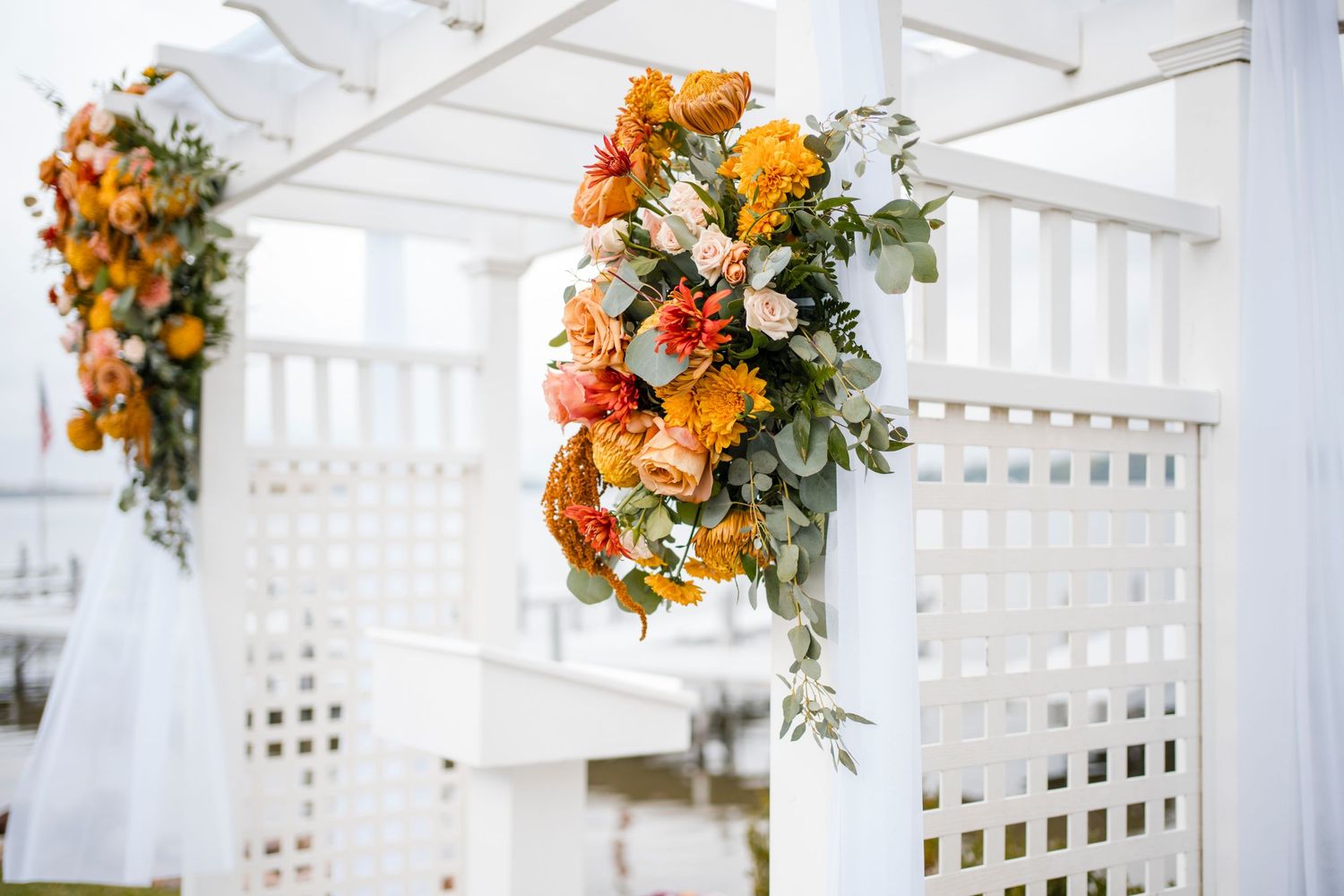 Orange and white floral arrangements hanging from white lattice wedding arch.