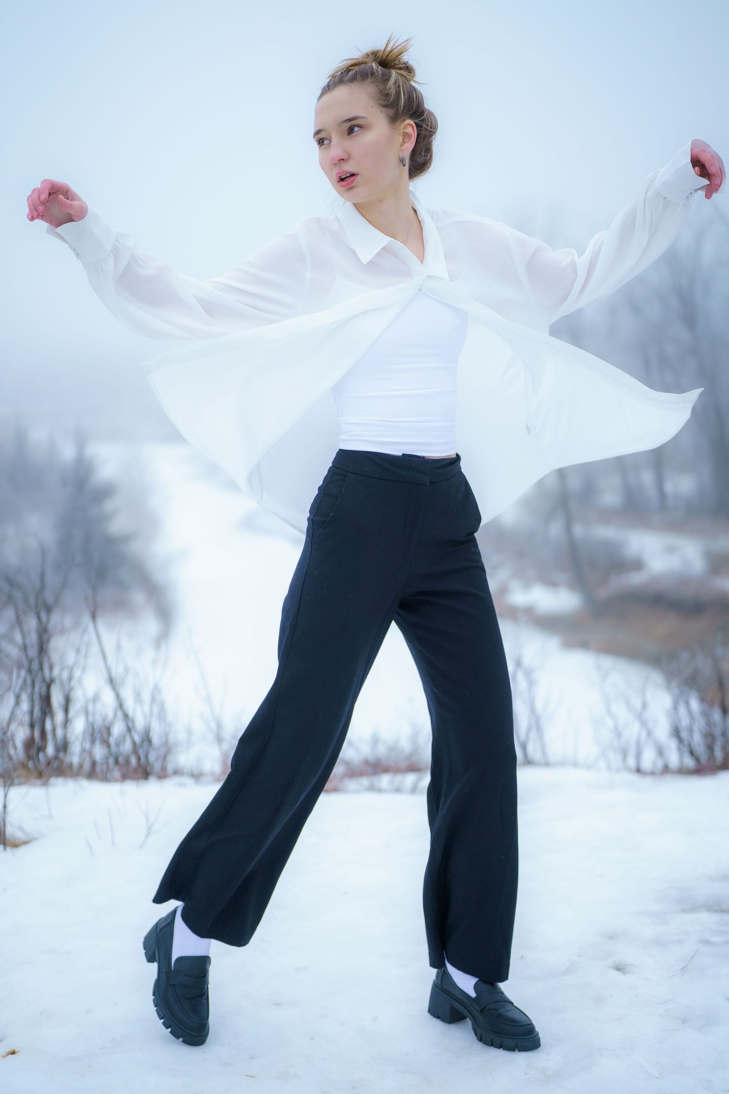 A graceful dancer in a white shirt and black pants performs an elegant pose against a snowy winter landscape.