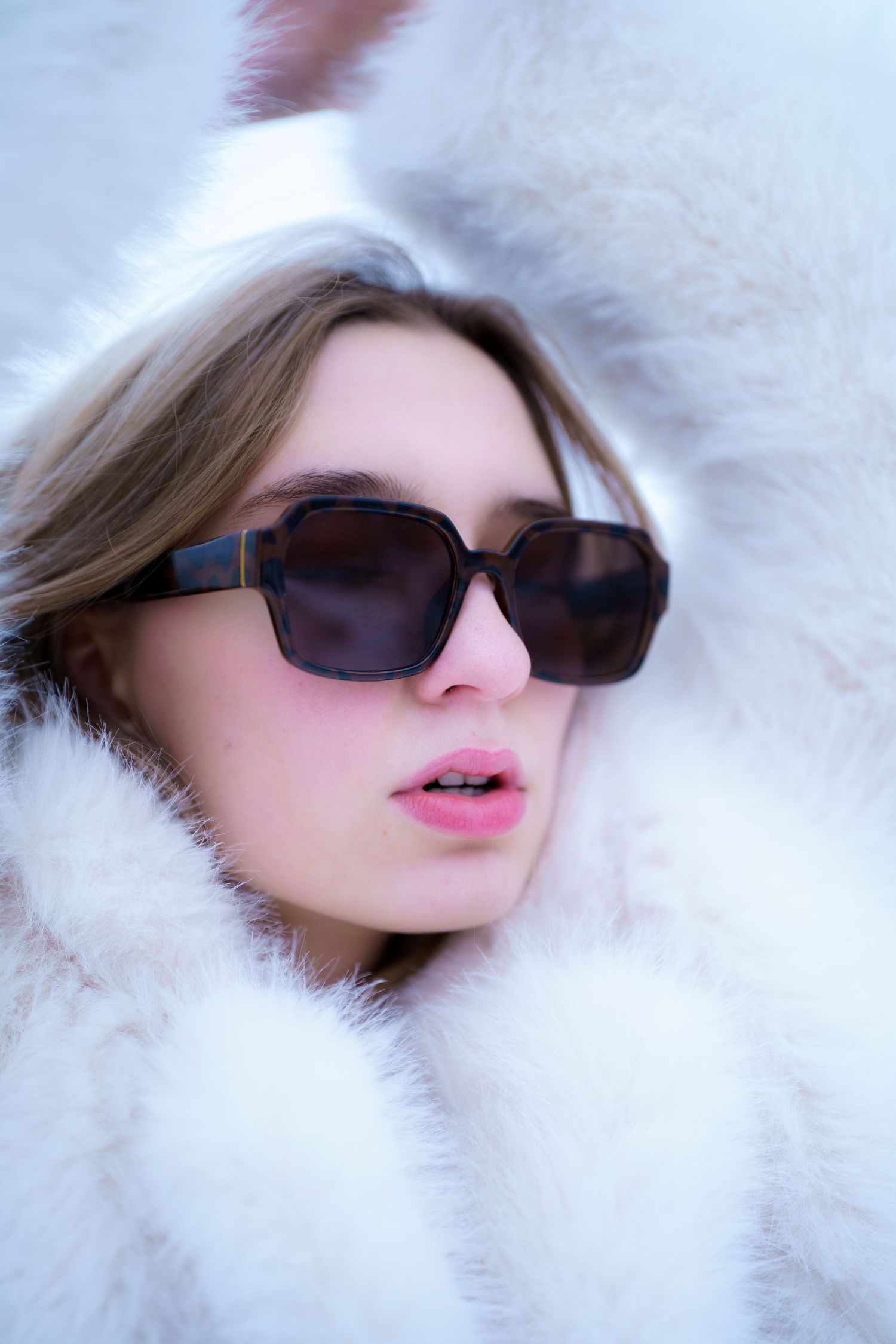 Fashion portrait with dark sunglasses and luxurious white fur coat in winter setting.
