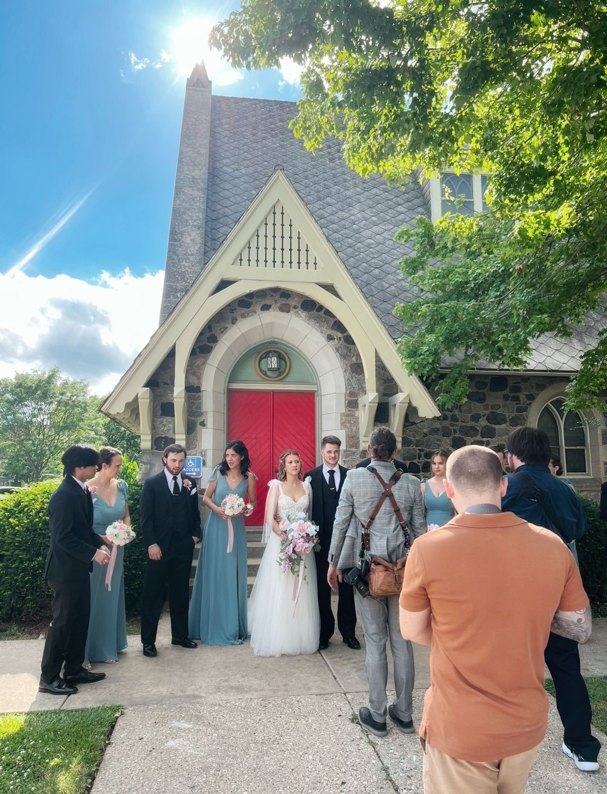 Wedding party gathered outside a charming church with Gothic architecture and red door.