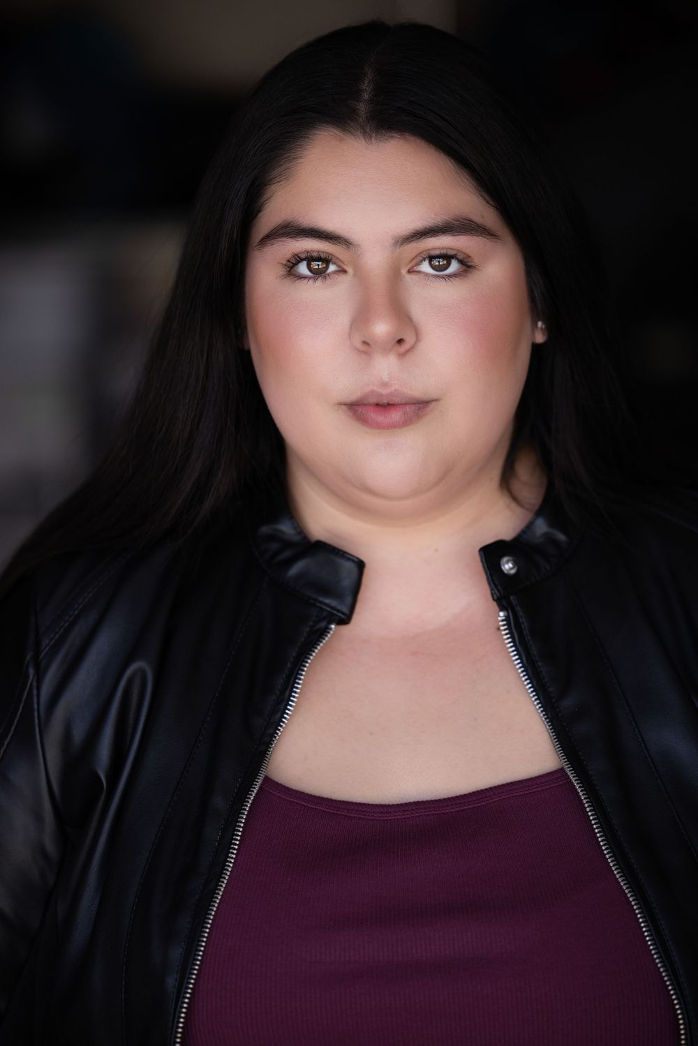 Portrait of person in black jacket and burgundy top.