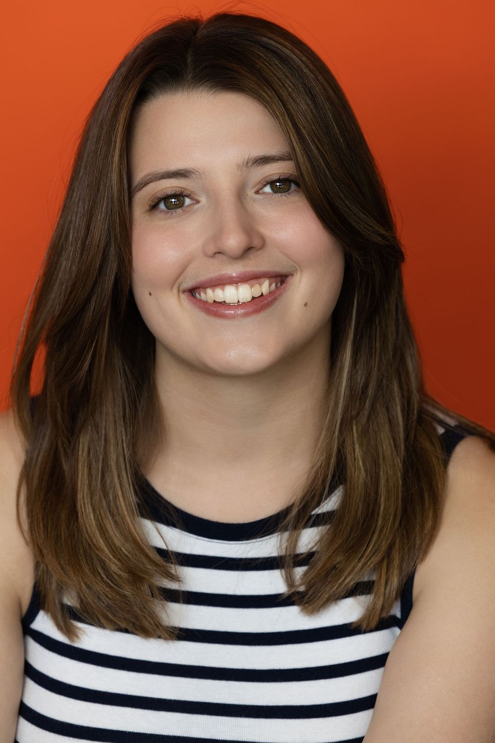 A person wearing a black and white striped sleeveless top poses with joyful expressions against an orange background.