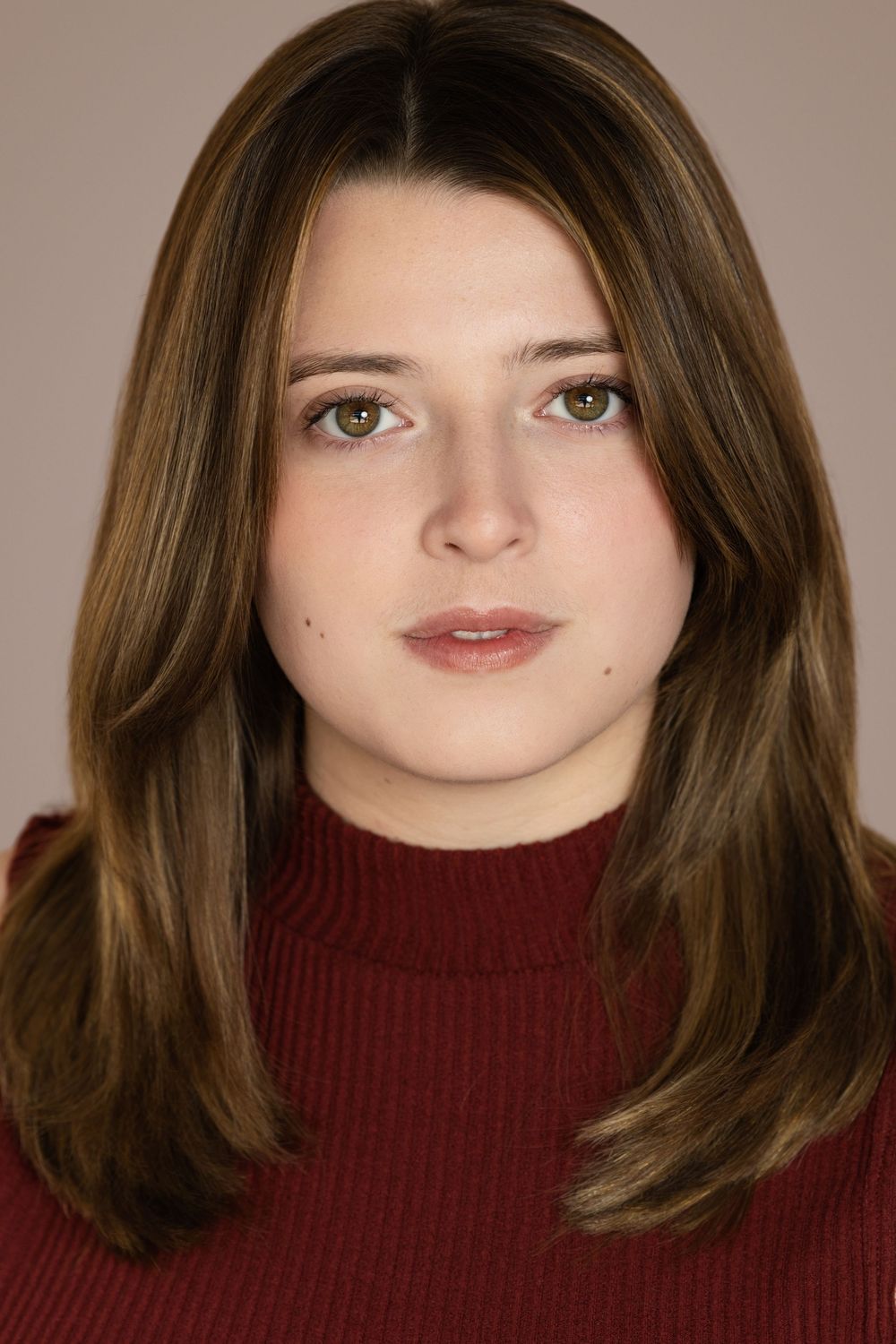 Professional headshot portrait in burgundy turtleneck sweater with long brown hair against neutral background.