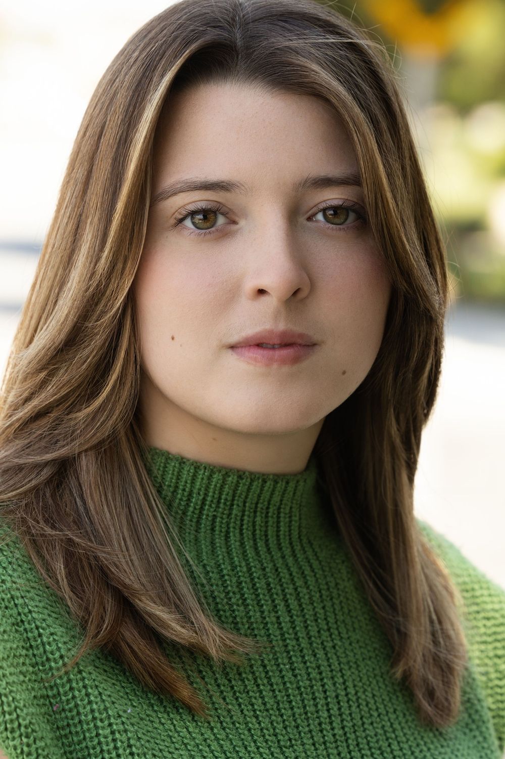 A person in a green knit turtleneck sweater poses for a portrait outdoors with soft natural lighting.