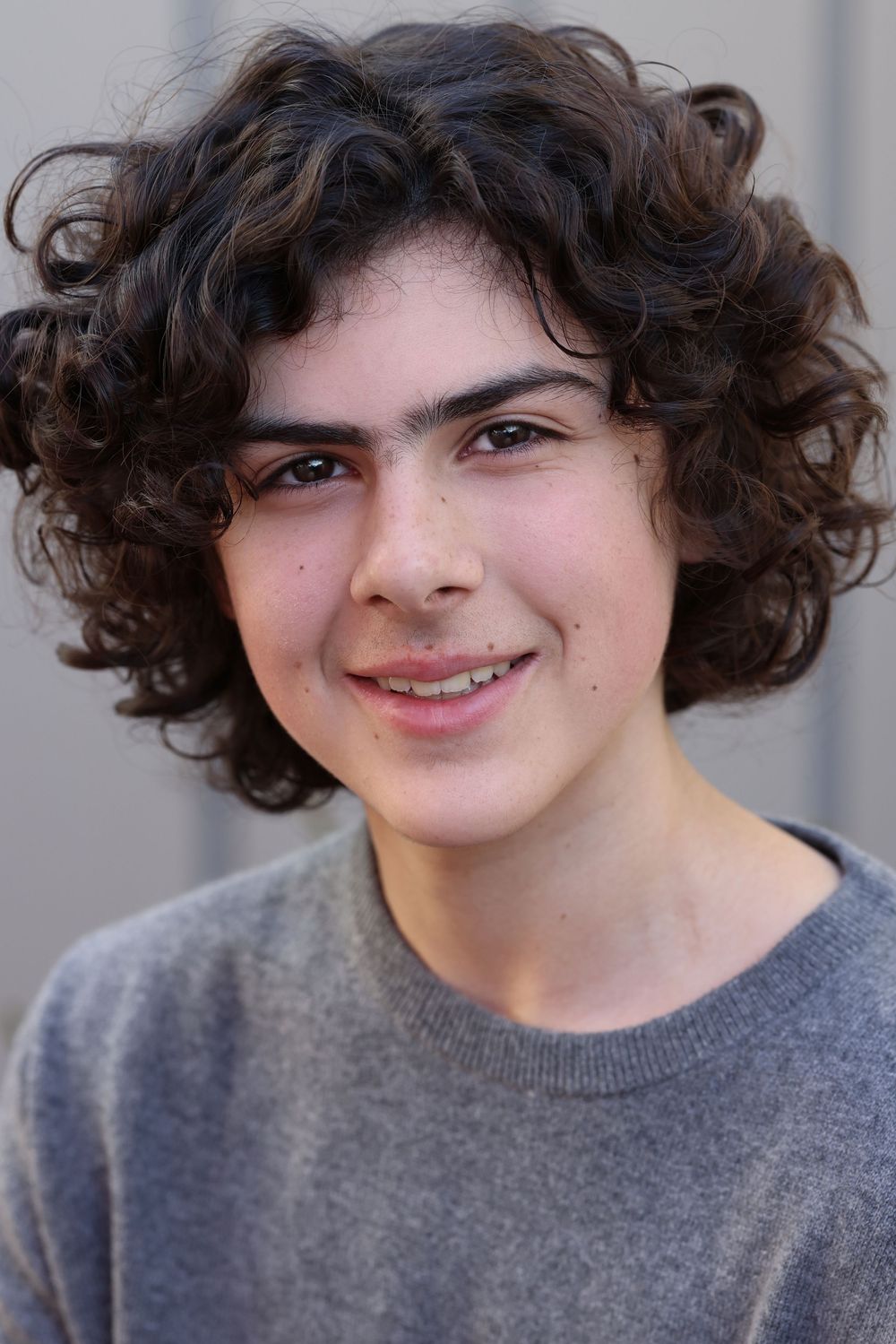 A montage of four close-up shots showing someone with curly dark hair and a grey sweater smiling at the camera.