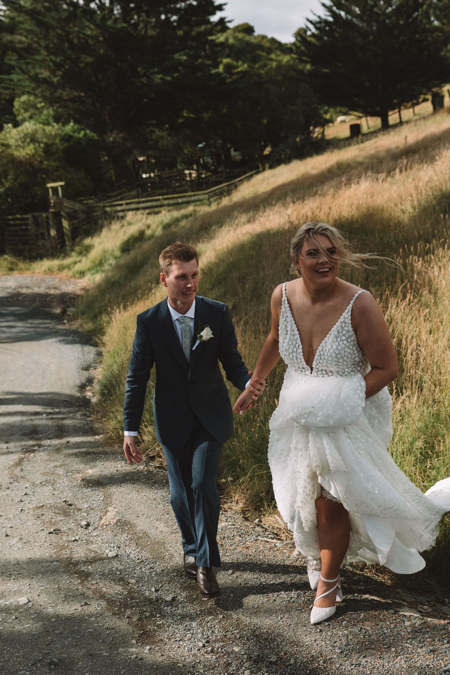 A cheerful couple walking down a countryside path after their wedding ceremony.