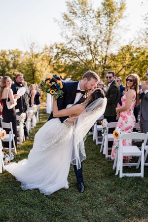 A wedding couple sharing a dramatic dip kiss during their outdoor ceremony.