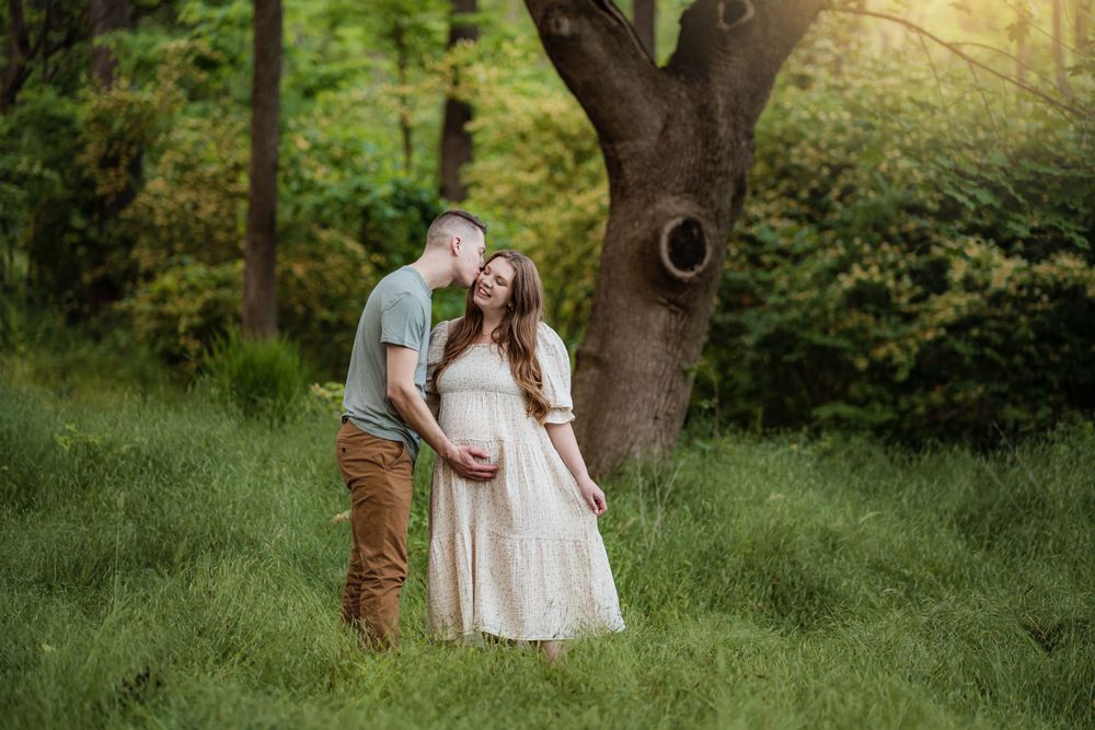 A romantic maternity photo shoot in a lush green forest setting at sunset.