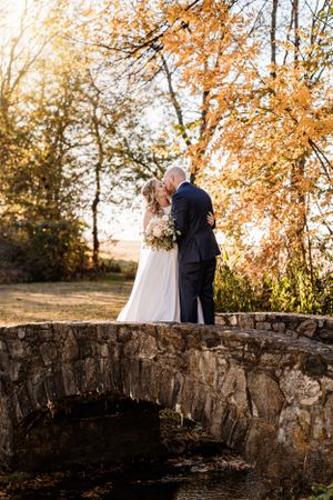 A couple sharing a romantic moment on a stone bridge during golden hour with autumn foliage.
