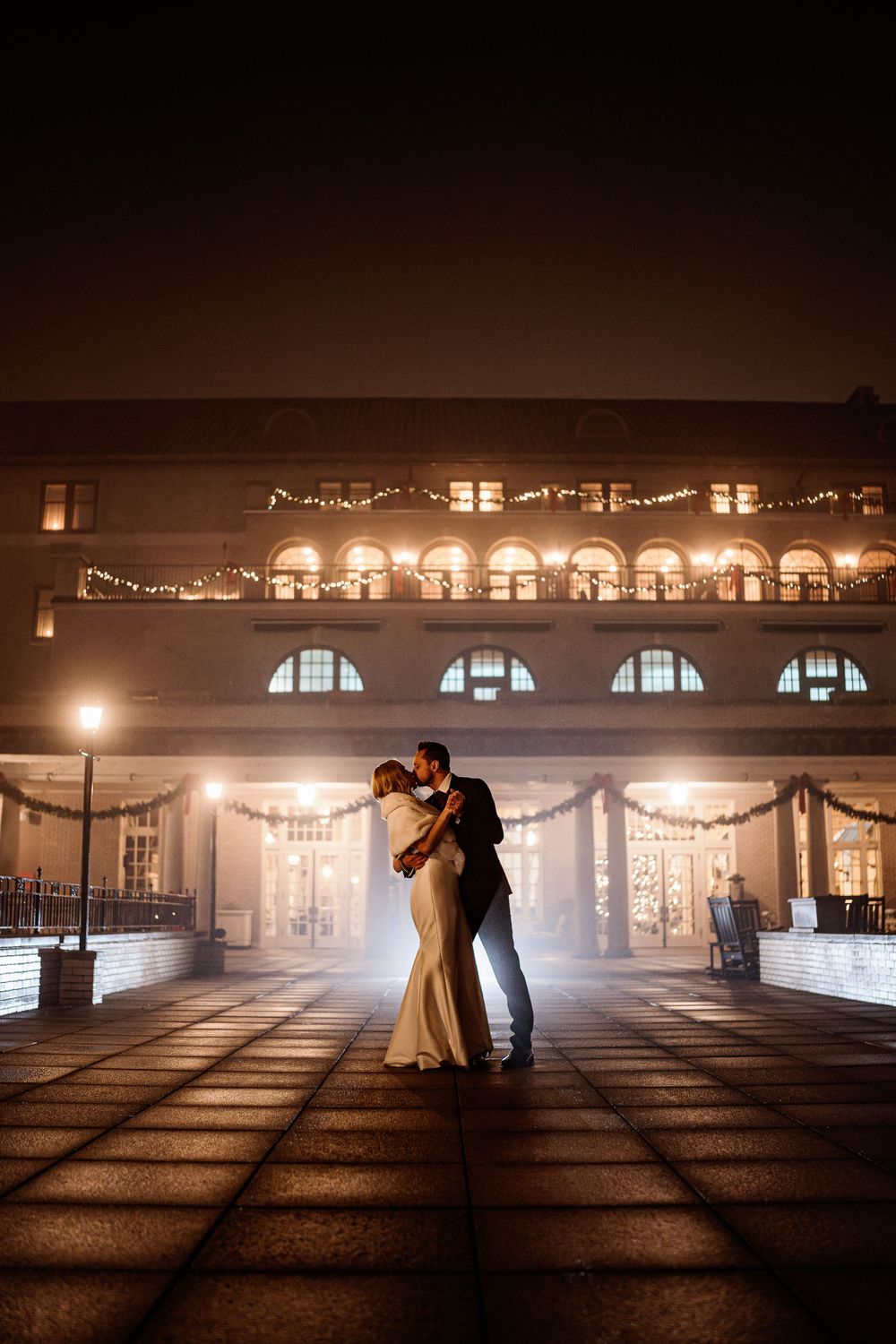 A romantic nighttime dance pose outside an elegantly lit building with arched windows.