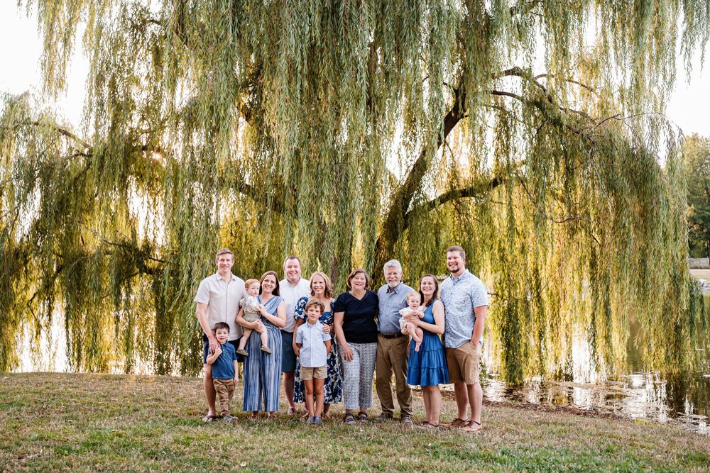 Extended family posing together under a dramatic weeping willow tree for outdoor portraits.