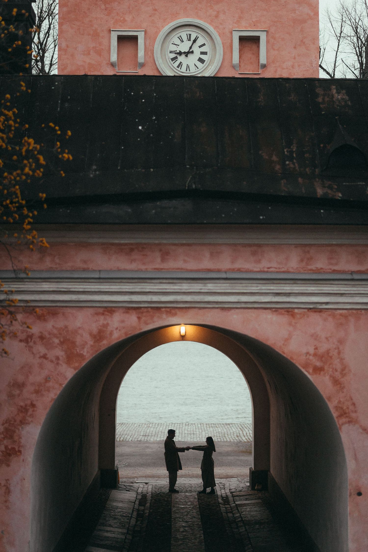 Silhouetted couple holding hands in arched passageway with clock tower above.