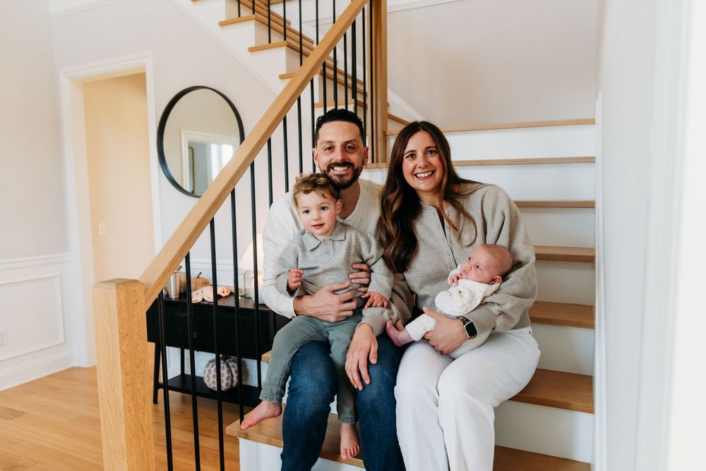 A family sits together on wooden stairs inside their home, featuring modern white walls and black metal railings.