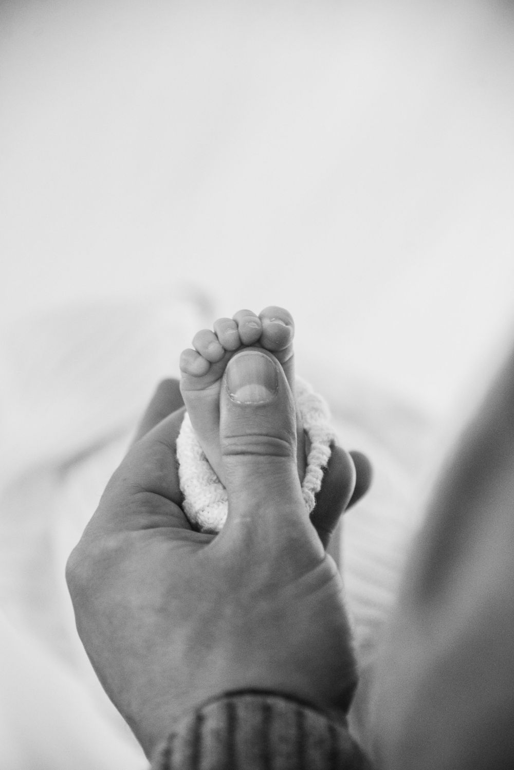 Black and white photo of an adult hand gently holding a tiny baby's foot in a tender moment.