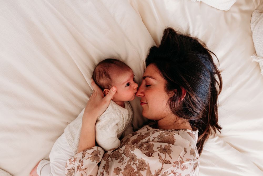 Tender moment captured from above as parent and baby lay together on white bedding wearing floral clothing.
