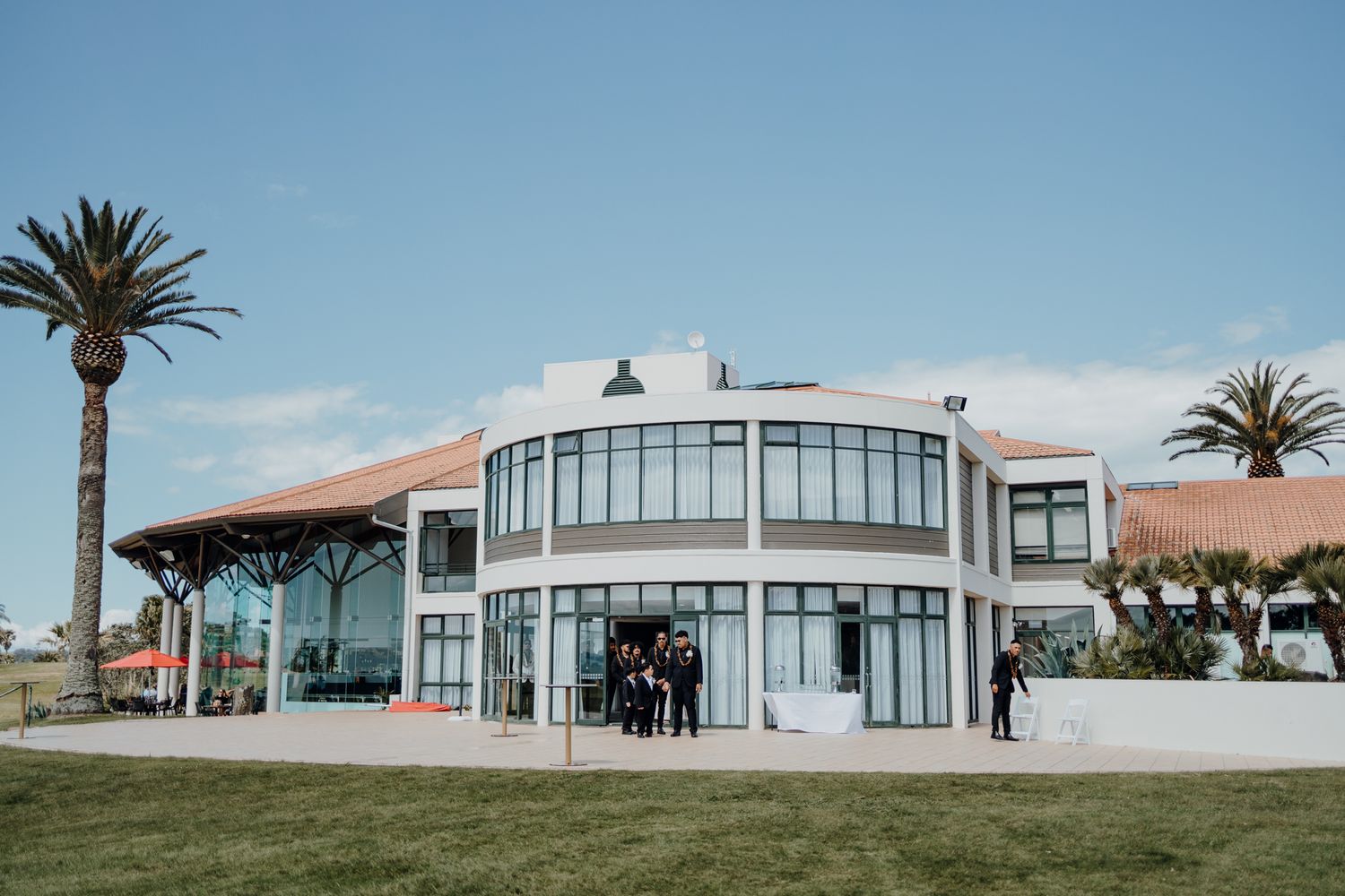 Modern white coastal wedding venue with curved glass windows and terra cotta roof.