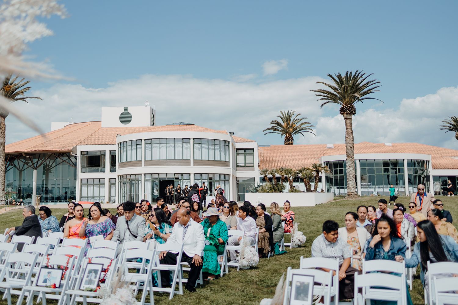 Outdoor wedding ceremony setup with white chairs and palm trees at a modern venue.