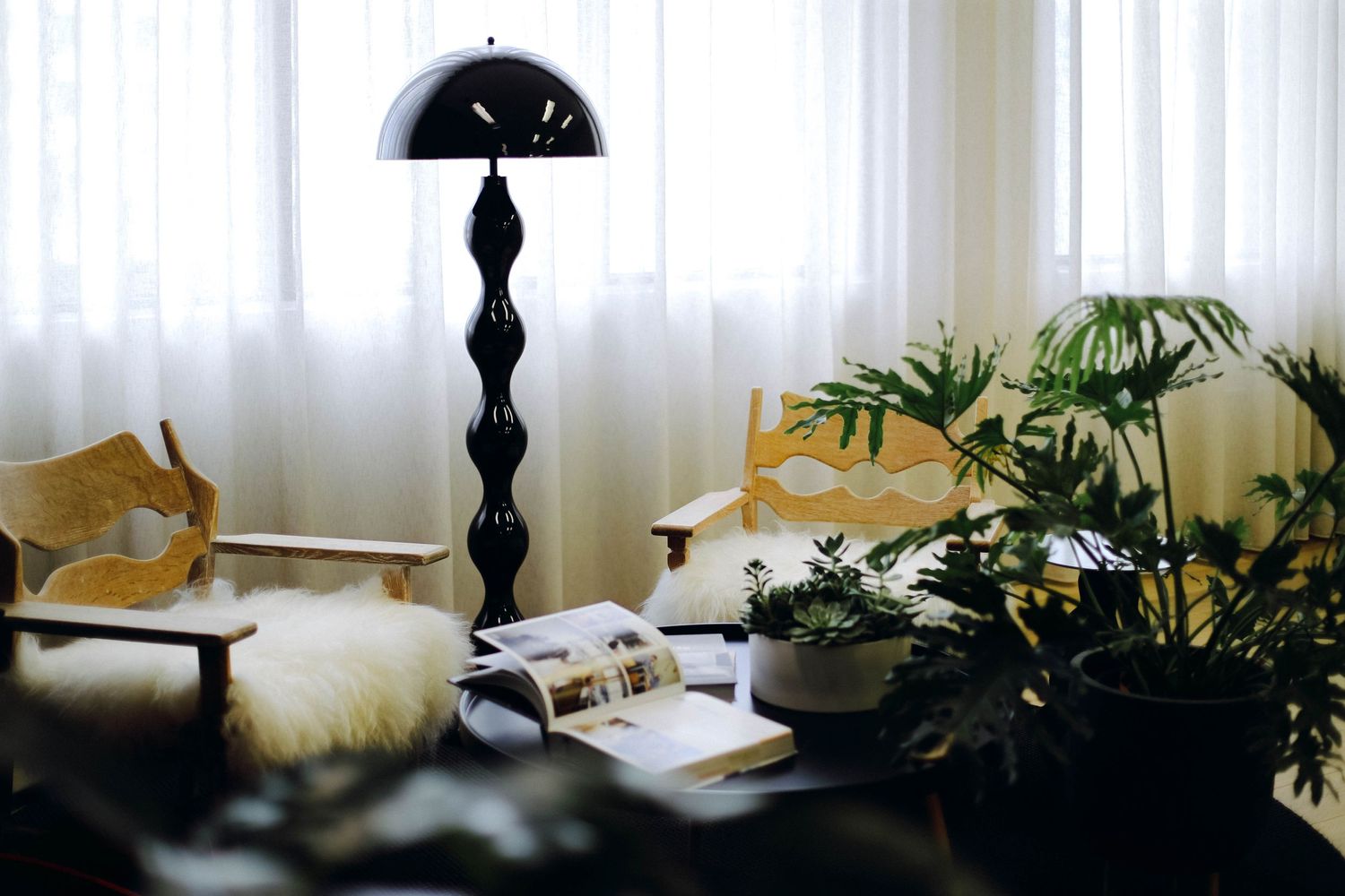 Cozy reading nook with black lamp, furry cushions, and indoor plants creating ambient atmosphere.