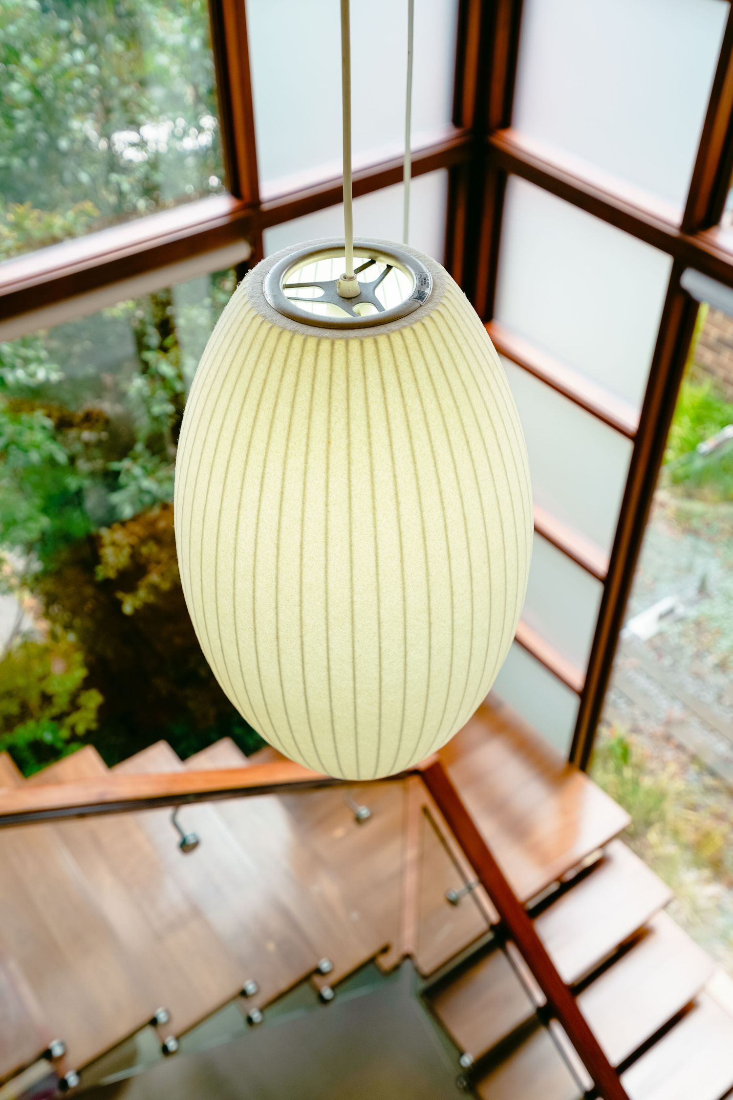 Elegant hanging rice paper lamp with ribbed texture above wooden staircase by window.