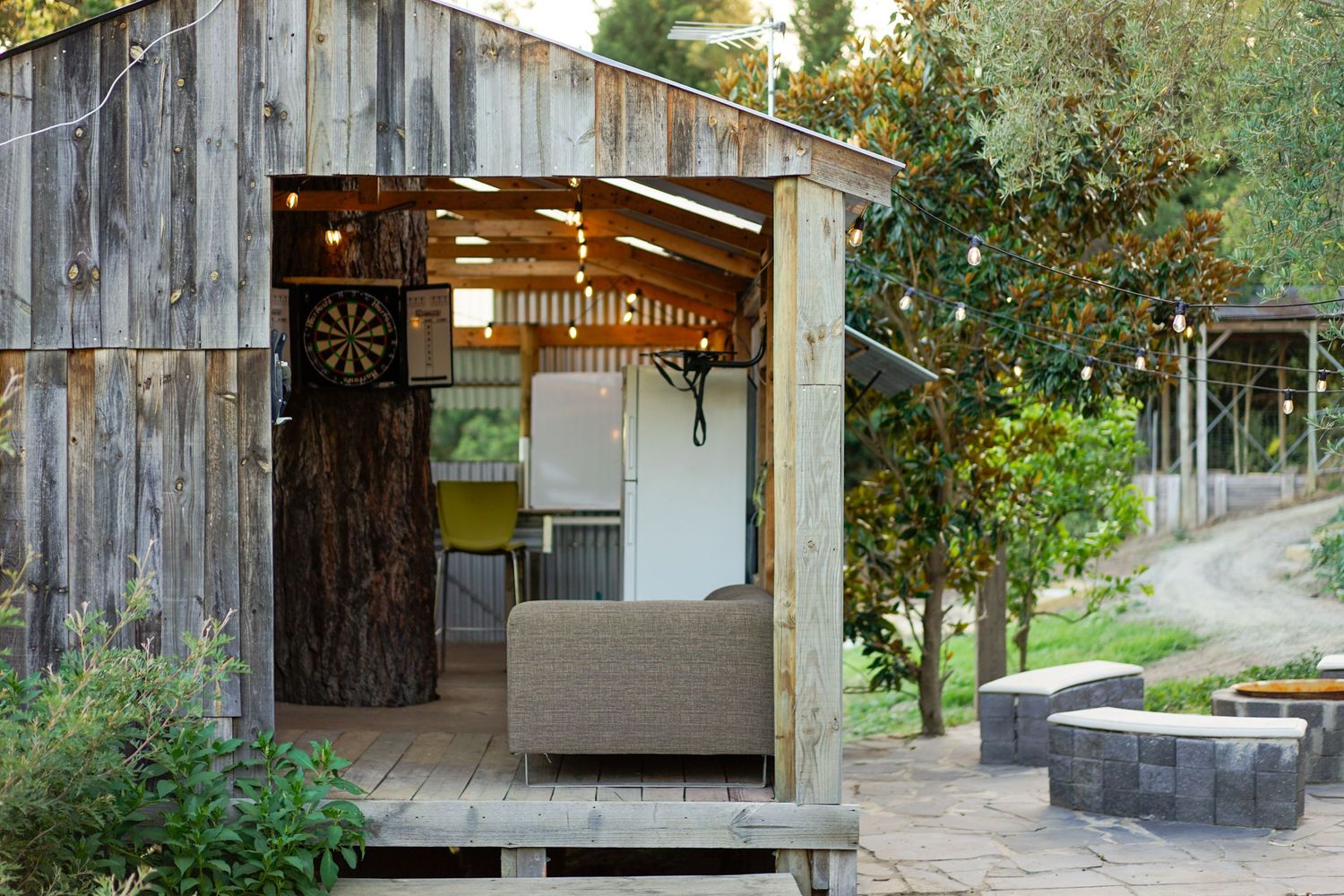 Rustic wooden shed converted into outdoor living space with string lights and fire pit.