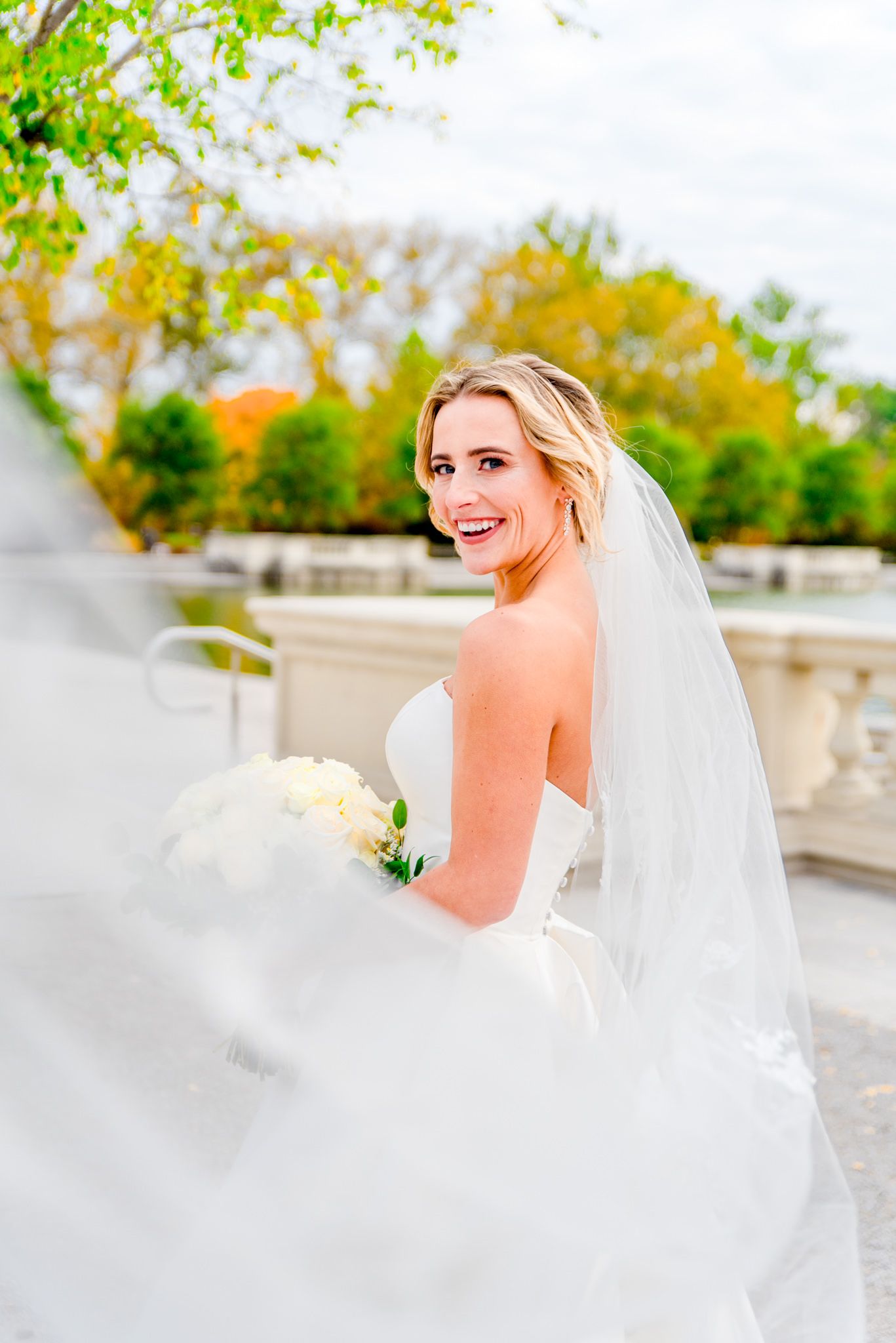 blonde bride with updo and long veil and white bouquet laughing at the camera for Forest Park STL wedding pictures