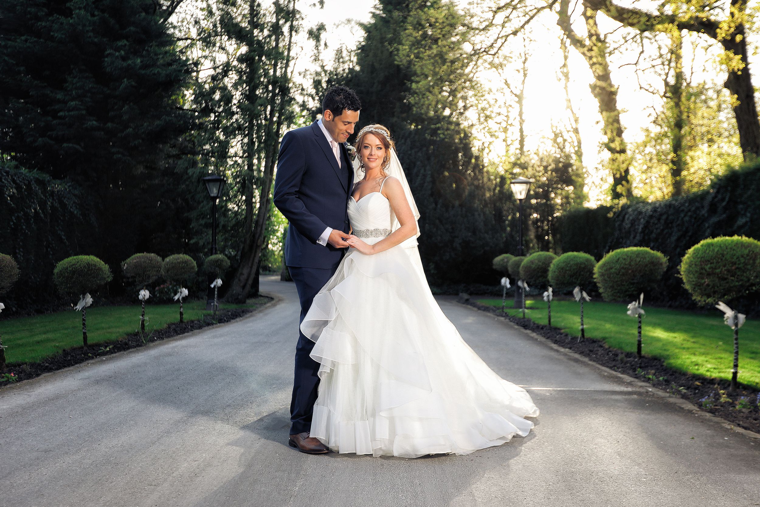 Groom wearing a smart suit holds his brides hand stood in the driveway at Bartle Hall wedding venue in Preston
