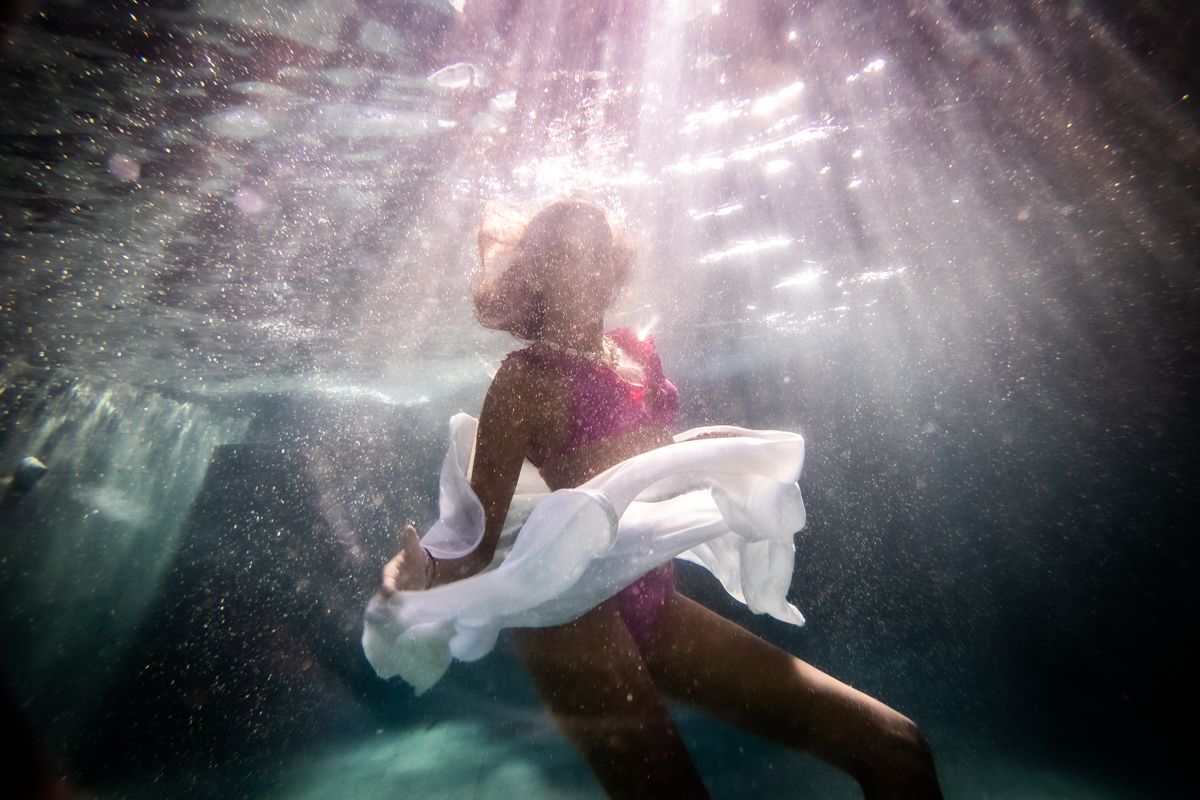 A silhouette of a woman underwater wearing a floating white skirt