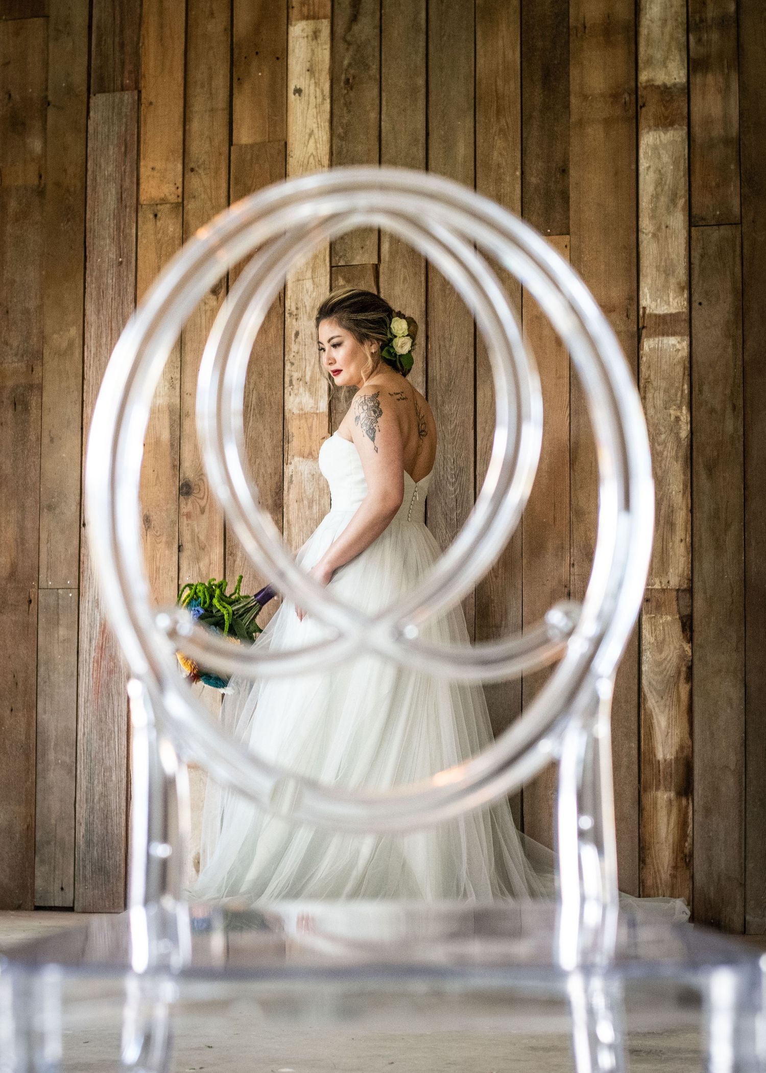 Asian woman stands behind a ghost chair holding a sola wood bouquet in a wedding dress