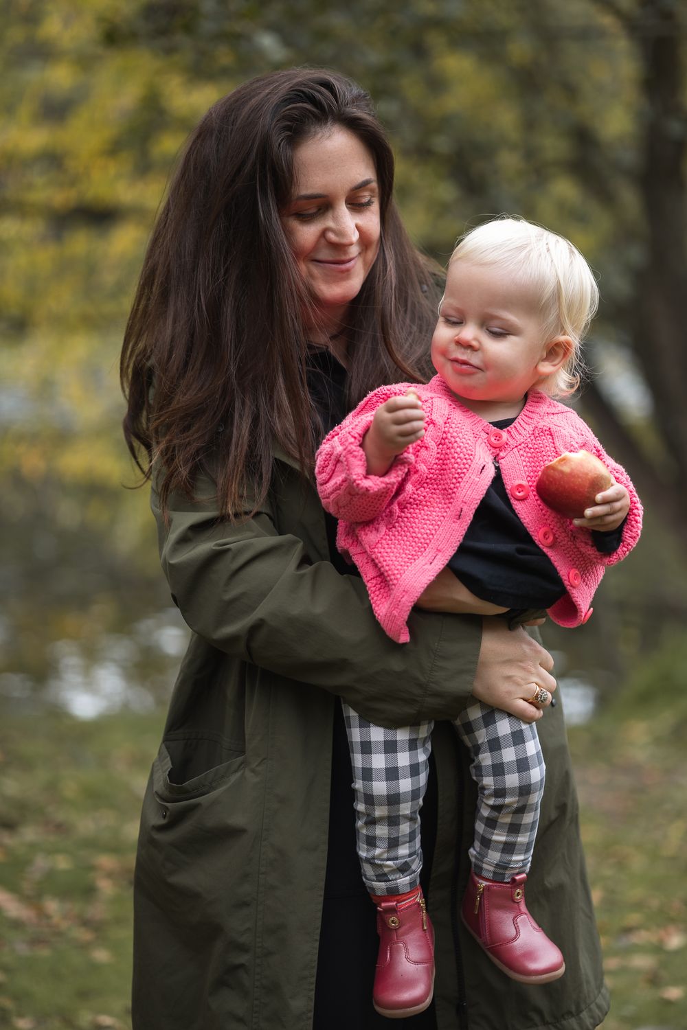 Mother carrying toddler eating an apple in North London Park